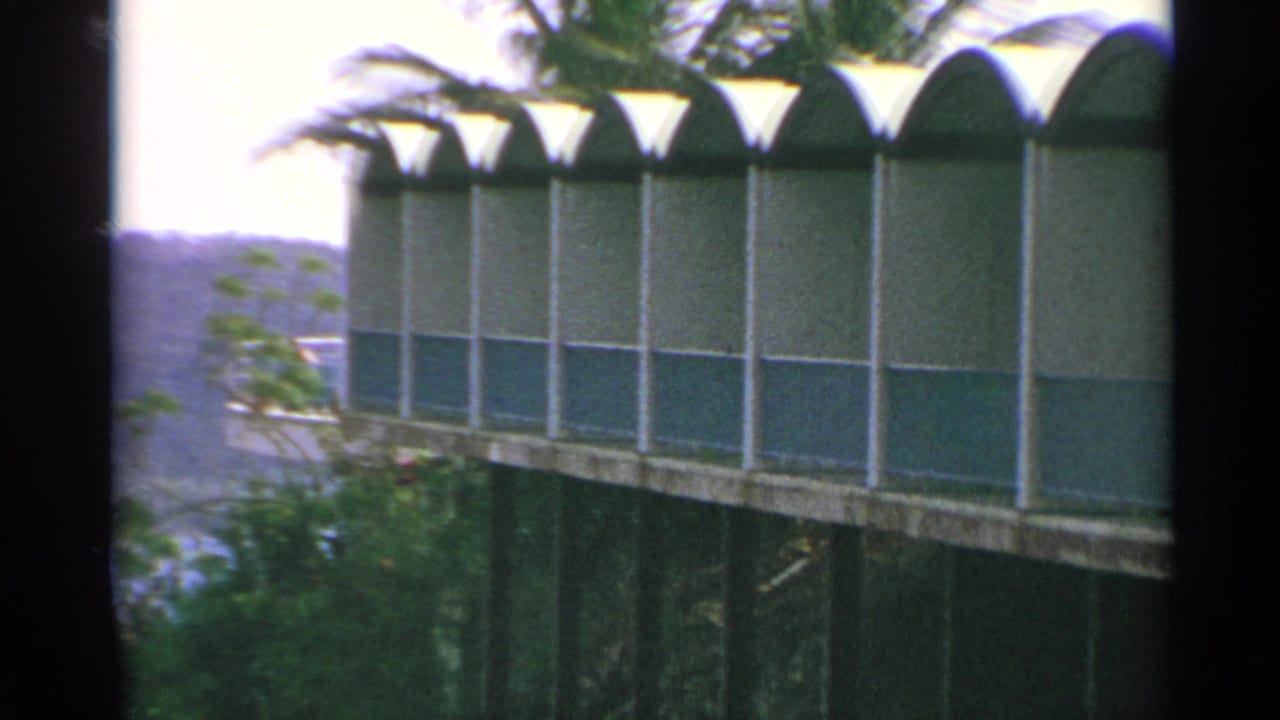 1967 US Virgin Islands home-movie frame showing a green-and-white arched glass facade viewed from a slightly elevated angle.