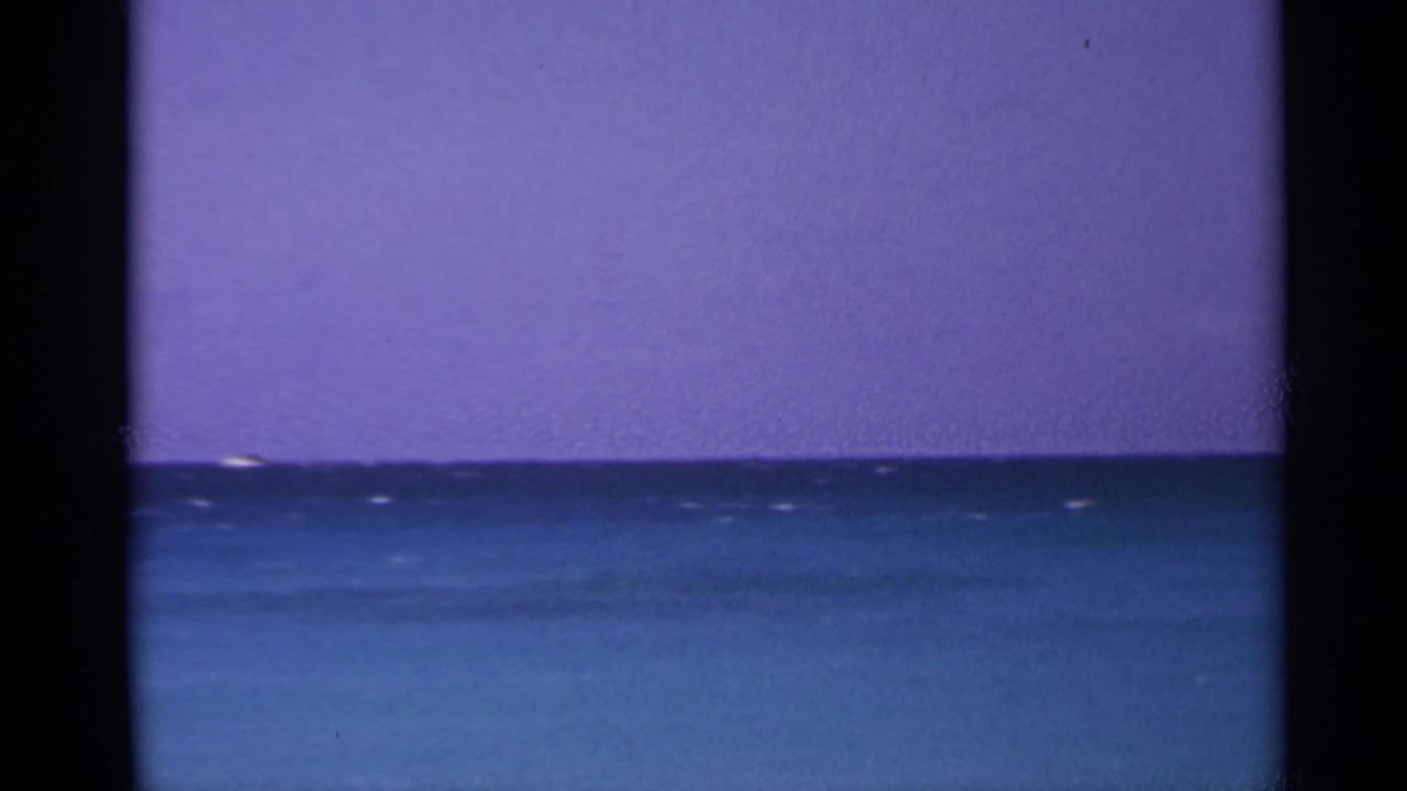 1967 US Virgin Islands 8mm view of a calm ocean horizon under a saturated purple sky, framed by dark scan borders.