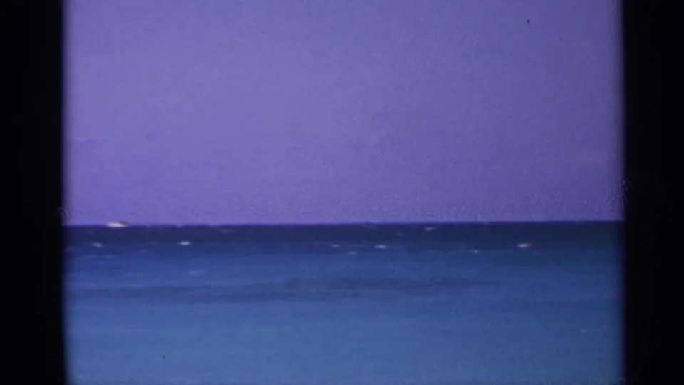 1967 US Virgin Islands 8mm view of a calm ocean horizon under a saturated purple sky, framed by dark scan borders.
