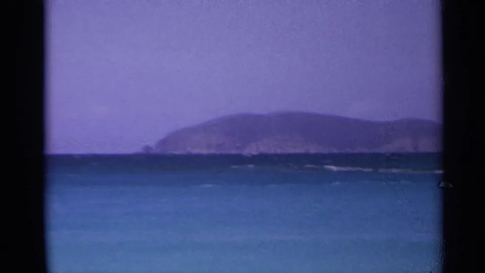 1967 US Virgin Islands 8mm frame with distant island hills on the horizon, blue water in front, and a saturated purple sky above.
