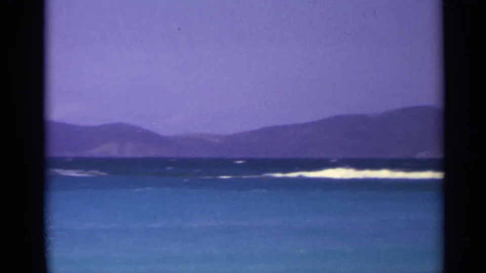 1967 US Virgin Islands 8mm view of island hills beyond blue water, with a bright band of breaking surf near the horizon.