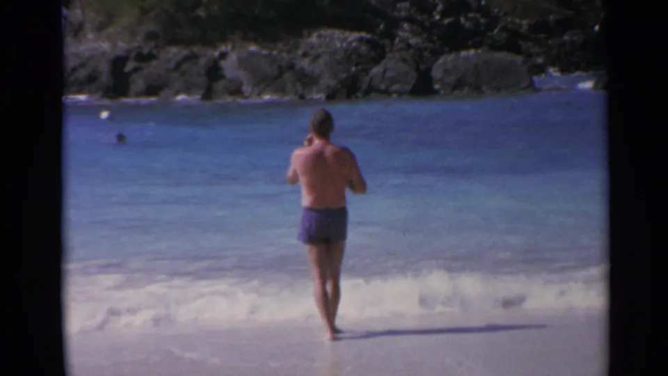 Rear view of a barefoot man at the shoreline, filmed in 1967 8mm home-movie footage from the US Virgin Islands.