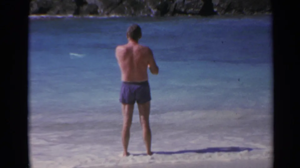 Closer 1967 8mm frame of a man in purple swim trunks standing at the edge of turquoise water in the US Virgin Islands.