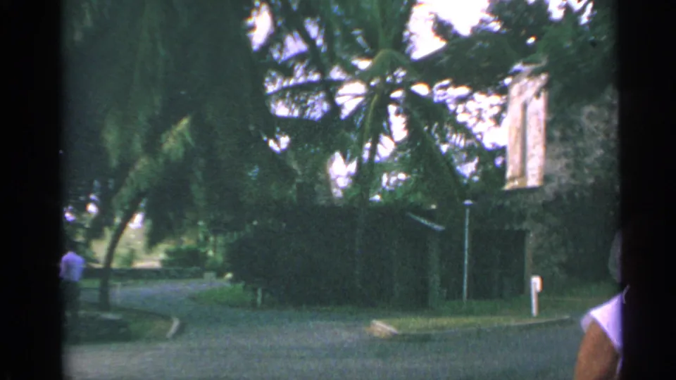 US Virgin Islands resort grounds appear in a 1967 8mm frame with palms, a paved drive, a low building, and a partly visible visitor at right.