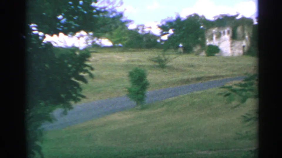 The 1967 rural US Virgin Islands view opens to a grassy slope with a winding gravel path and a distant pale stone building.