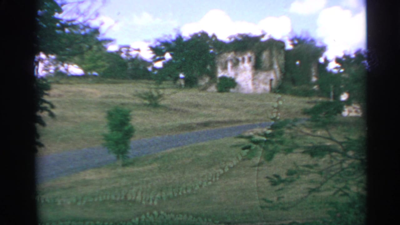 1967 US Virgin Islands home-movie view of a grassy slope, curving path, and castle-like stone ruins framed by trees.