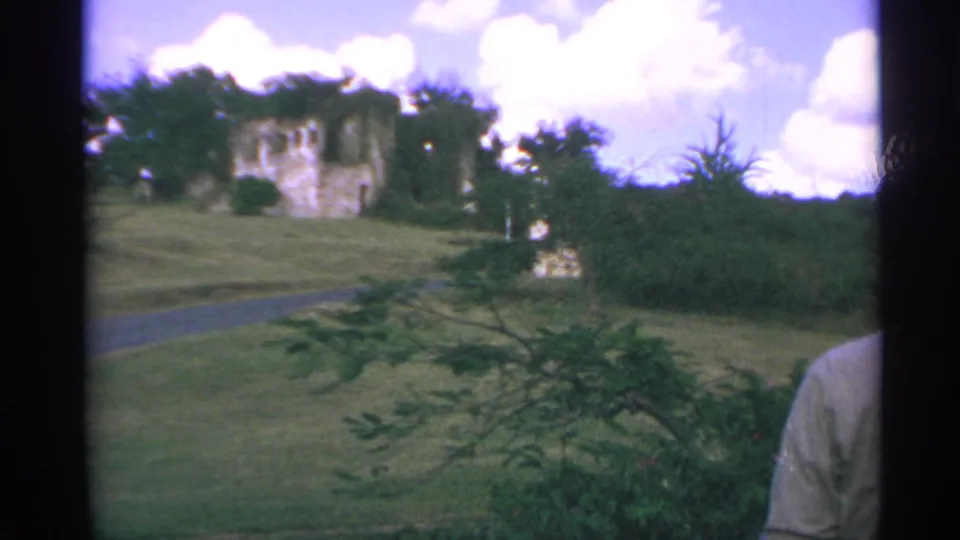 US Virgin Islands travel footage shows hillside ruins, a curving path, trees, and a partially visible traveler at frame edge.