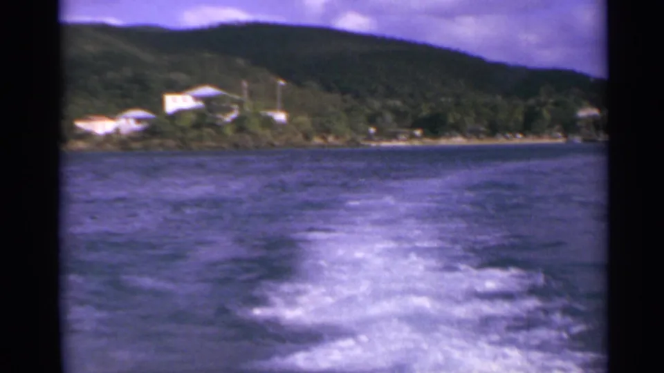 US Virgin Islands boat view with white wake crossing blue water toward a green shoreline with scattered buildings.