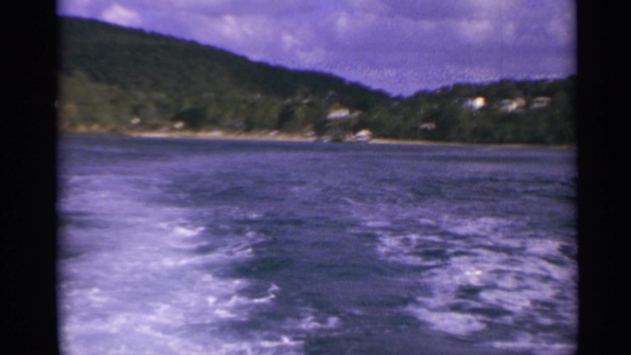 Wide wake behind a boat with wooded shoreline and small houses in the distance.