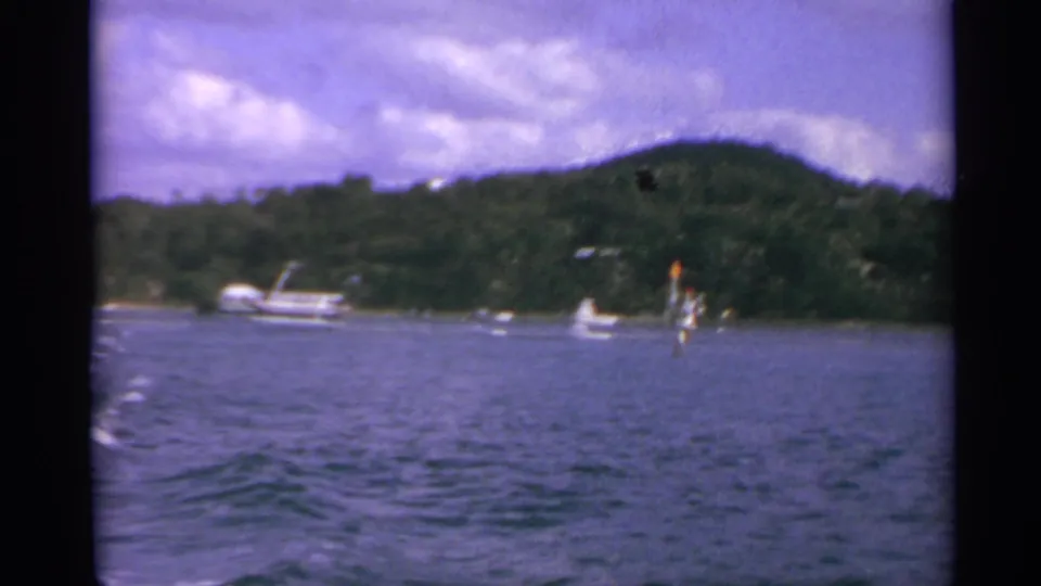 Final 1967 8mm frame from the US Virgin Islands, showing a broad water view, wooded hillside, boats, and visible film softness.