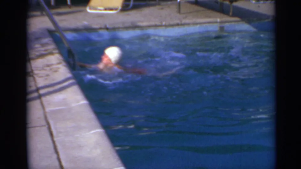 A poolside view shows the swimmer nearing a metal ladder, with strong shadows across the concrete deck.