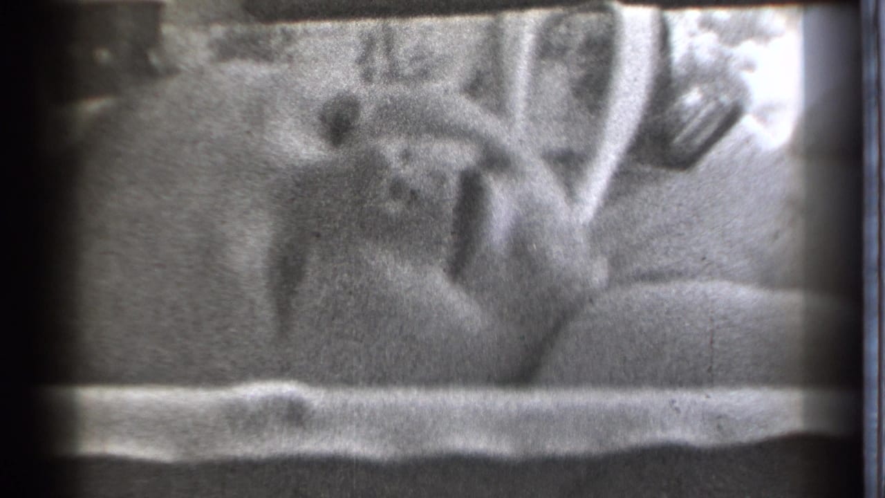 A baby lies in bed in Danielson, Connecticut, in 1939 home-movie footage, framed by bedding and dark film edges.
