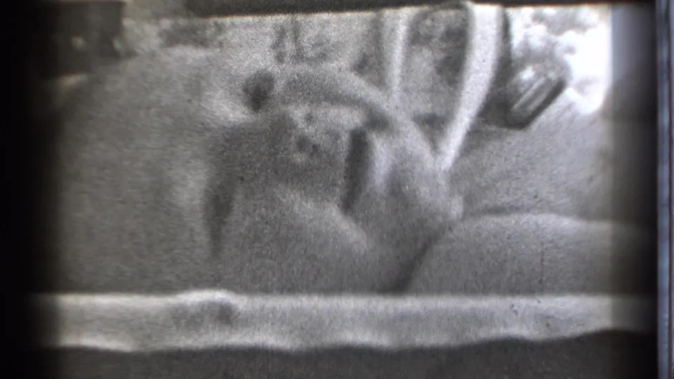 A baby lies in bed in Danielson, Connecticut, in 1939 home-movie footage, framed by bedding and dark film edges.
