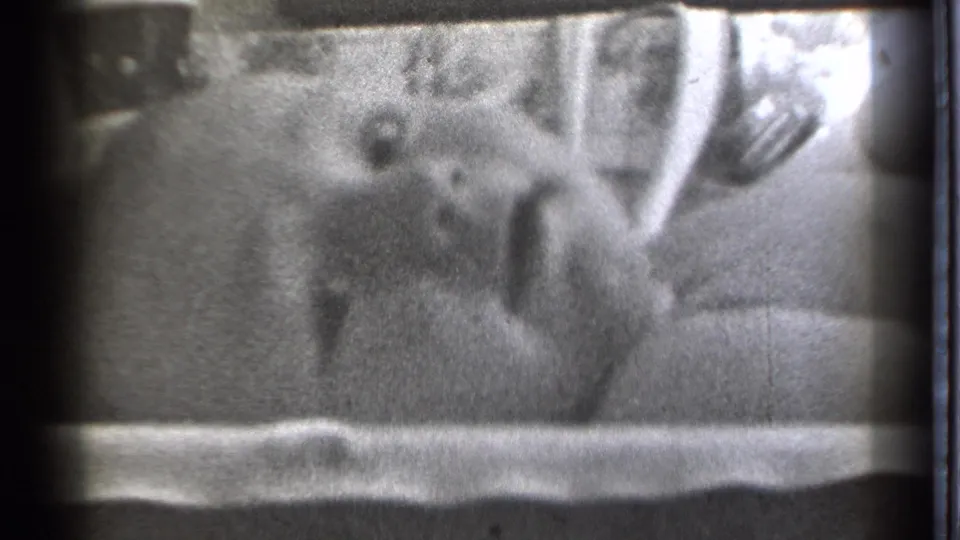 The infant rests on bedding and turns slightly within a grainy 1939 Danielson home-movie bedroom scene.