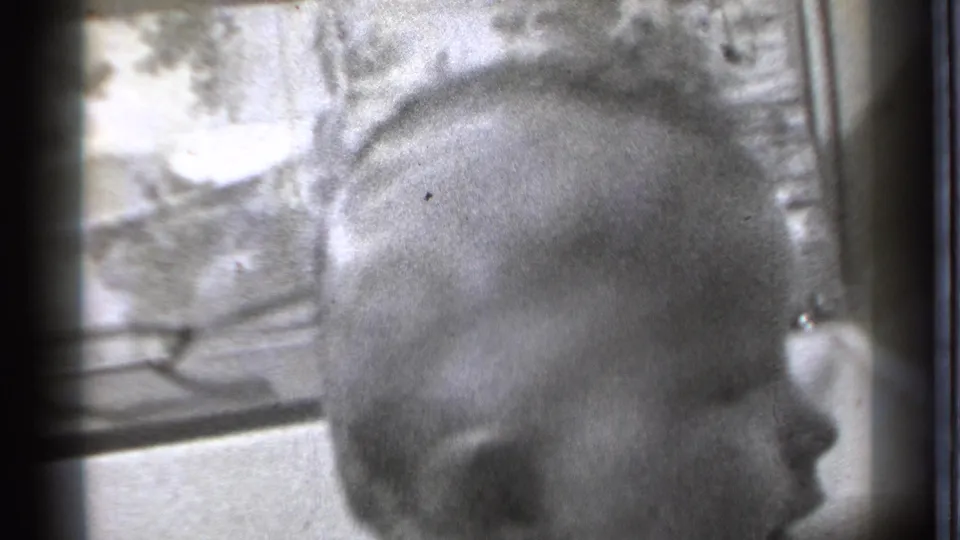 A close, soft-focus view shows the baby's head near a window area and bed frame in the Danielson home interior.