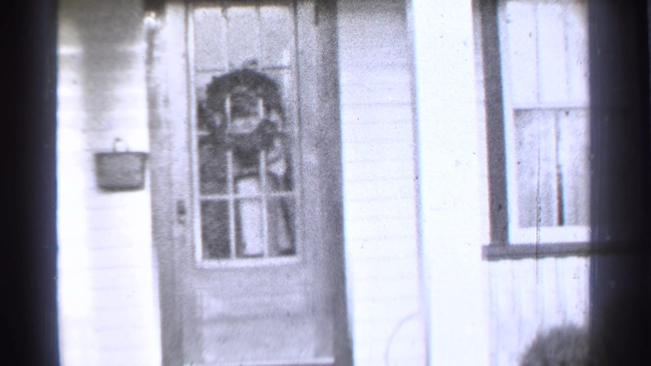 Front door and window of a white-sided house, with a wreath visible on the door.