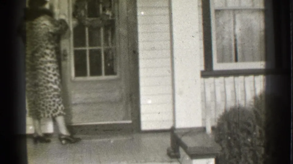 1939 Danielson, Connecticut frame with a woman in a patterned dress standing near the decorated front door of a white-sided house.