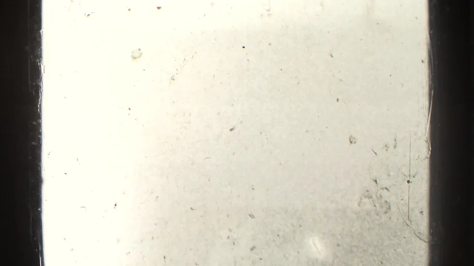 Overexposed 8mm frame with a dark vertical edge, faint exterior detail, dust, and surface marks from the physical film.