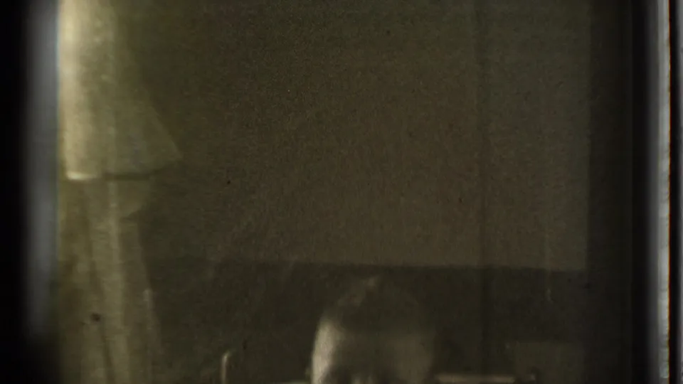 Dim 1939 home interior in Danielson, with curtains, shadowed walls, and a partially visible seated person near the lower frame.