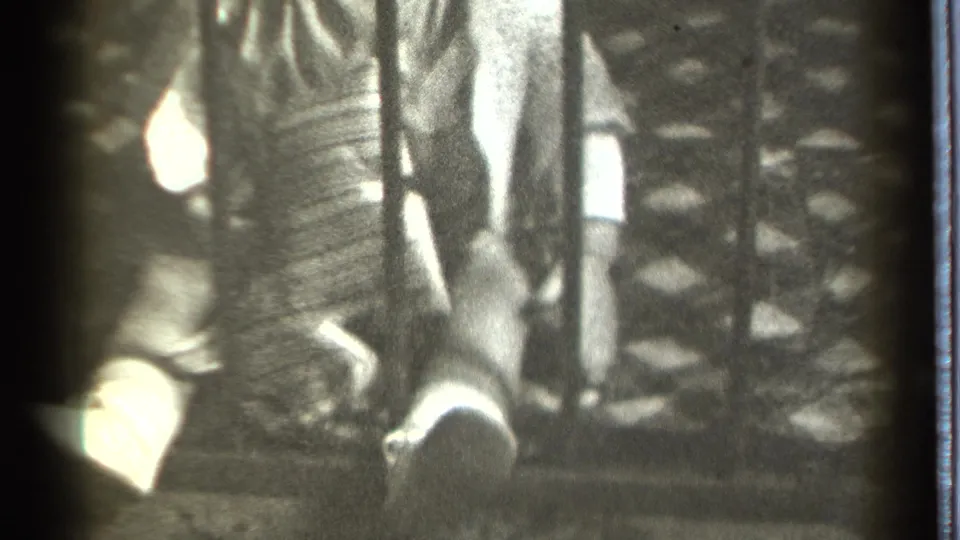 In 1939 Danielson home-movie footage, a baby in light clothing reaches toward and holds a dark vertical metal bar.