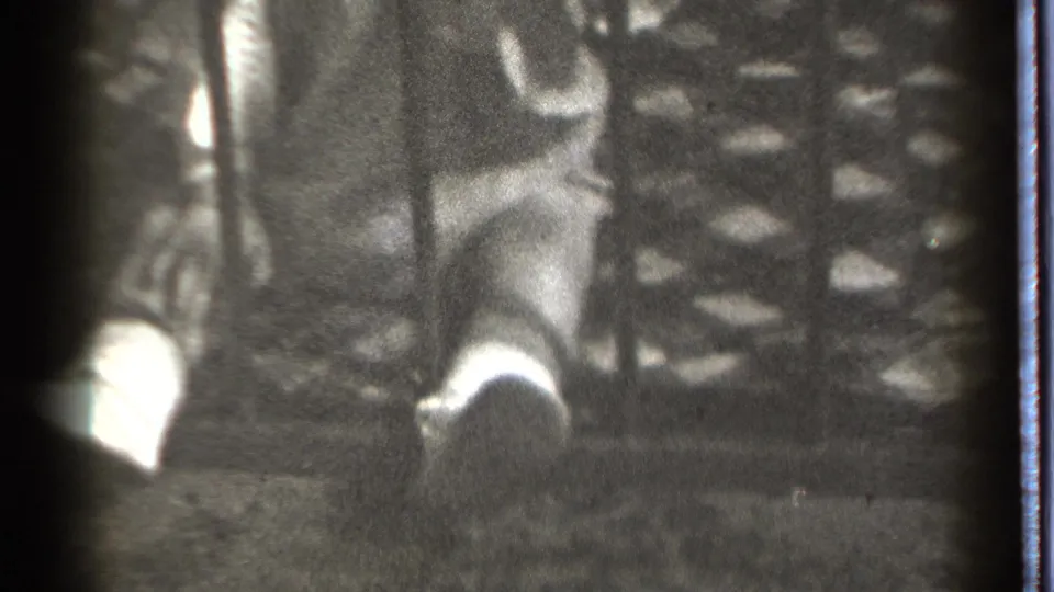 A close home-movie frame shows the baby partly obscured by blur and film grain while reaching near the vertical metal bar.
