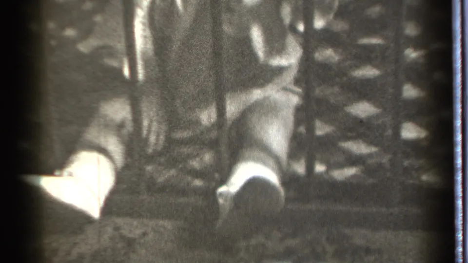 In 1939 Danielson home-movie footage, a seated child is partly visible behind vertical bars with light socks and fabric nearby.