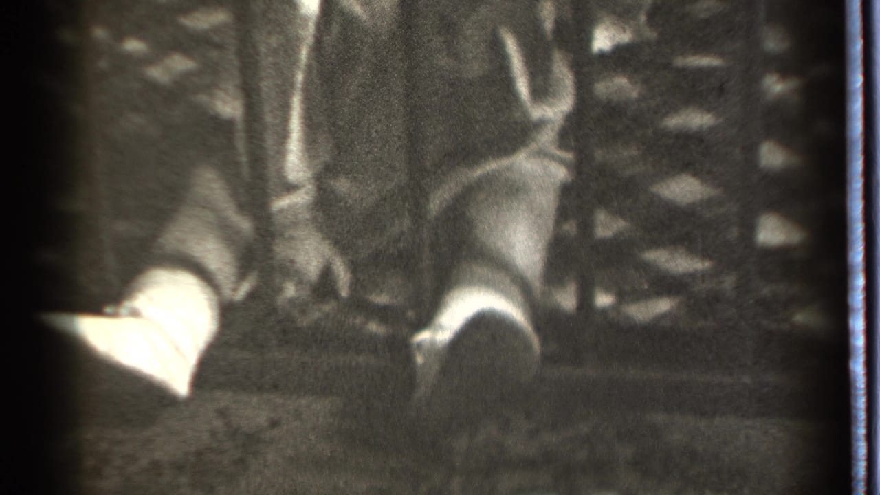 Child seated behind bars with feet forward and hands near dark fabric.