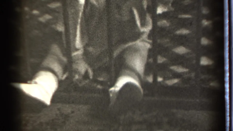 The child remains behind vertical bars in the Danielson 8mm footage, with feet forward and hands close to textured fabric.