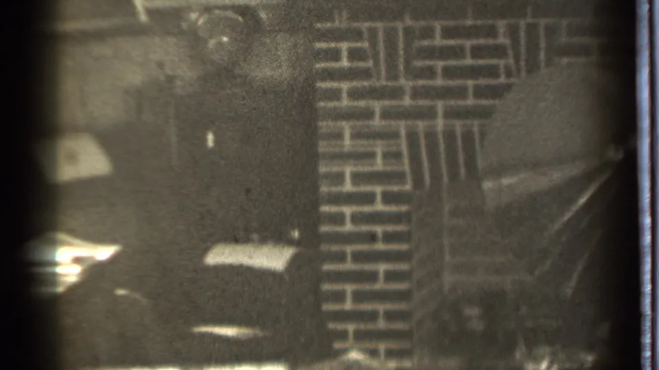 Grainy 8mm frame from a 1939 Danielson interior, centered on brickwork and a shadowed fireplace area.