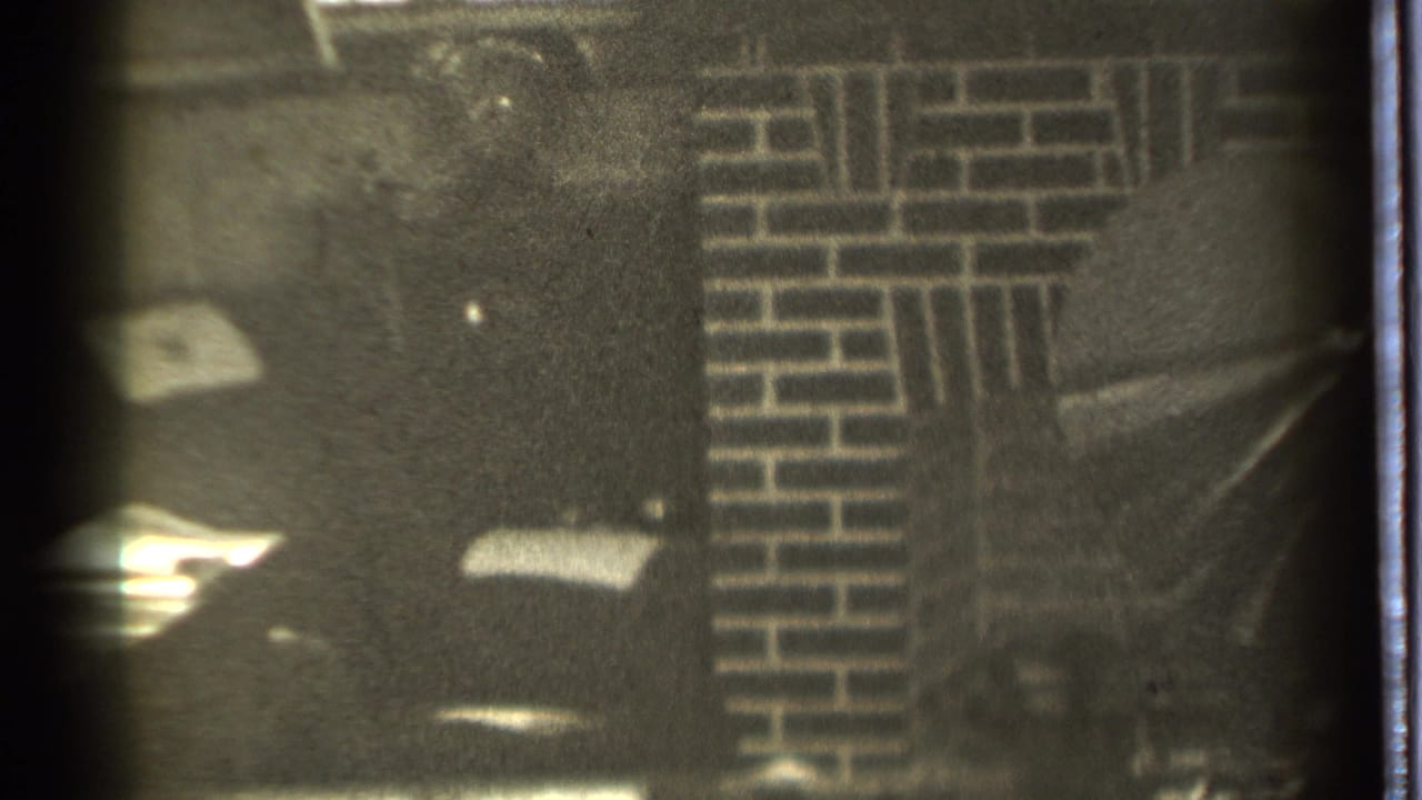 Dim interior with a man partly visible near a brick fireplace wall.