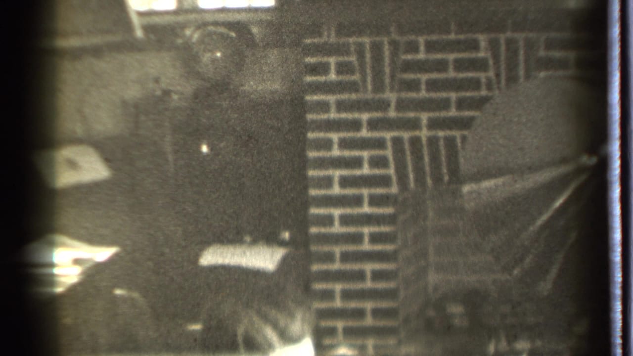 Man partly visible at the bottom of a dim room with brickwork behind him.