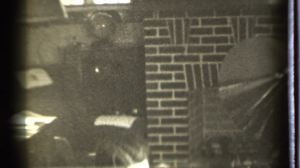 1939 Danielson 8mm frame with a man's head partly visible below dark wall surfaces and patterned brickwork near a fireplace.