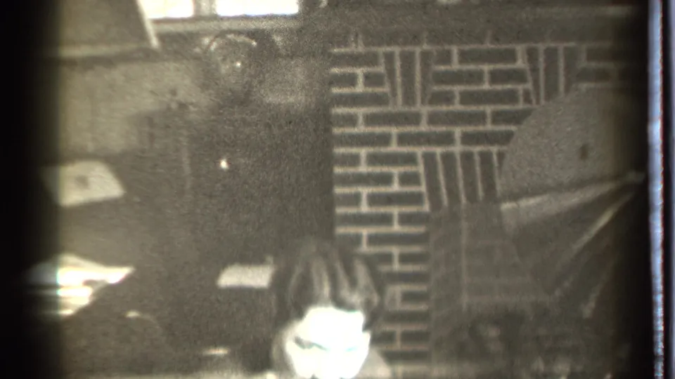 1939 Danielson frame showing a seated man bending forward in a dark room with visible brick fireplace detail and soft 8mm grain.