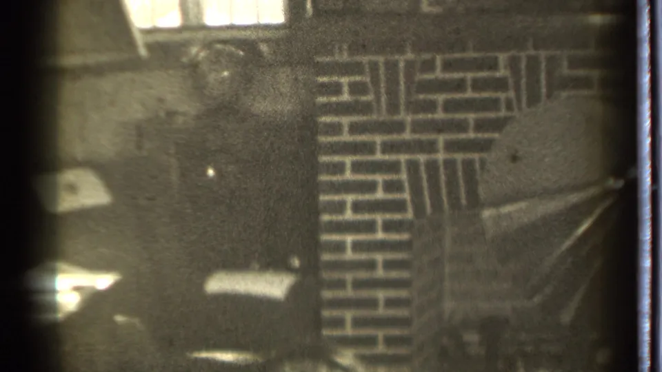 1939 Danielson 8mm frame of a dark domestic room, brick fireplace detail, and a man partly cropped at the lower edge.