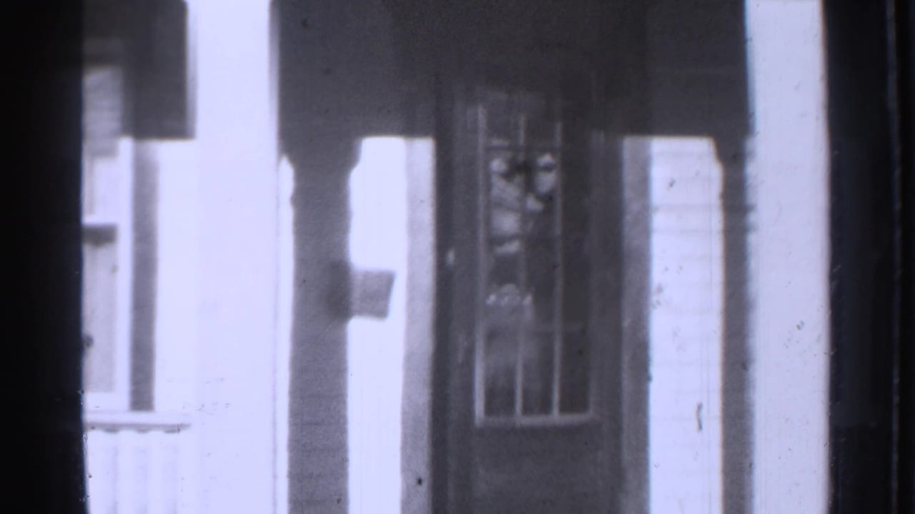 Porch doorway and window seen through dark film-frame borders, with no clear person visible.