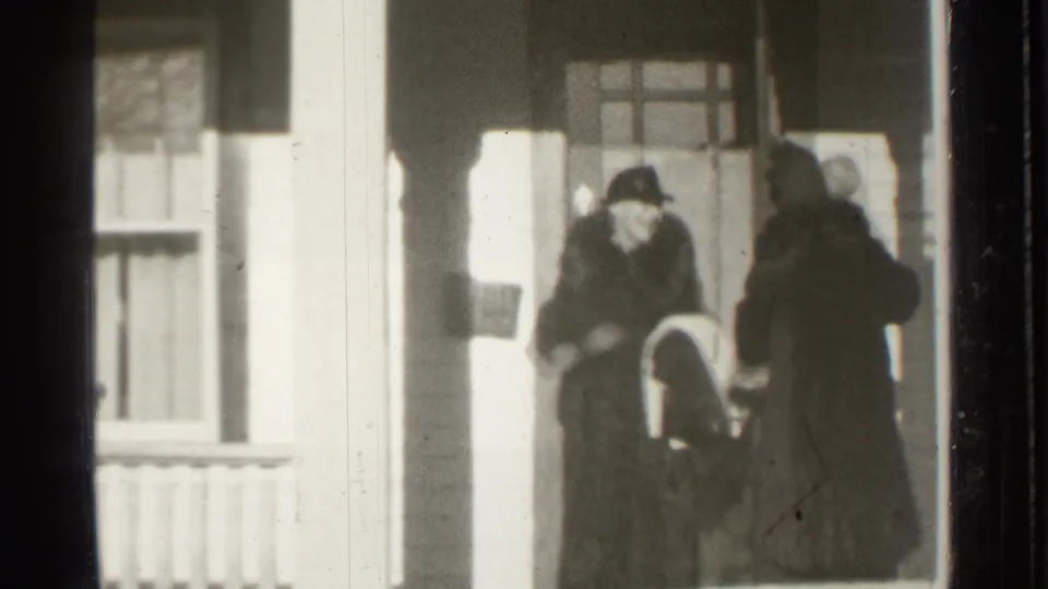 Adults in period coats and hats stand on a Danielson house porch in 1939, framed by columns, a window, and 8mm film edges.