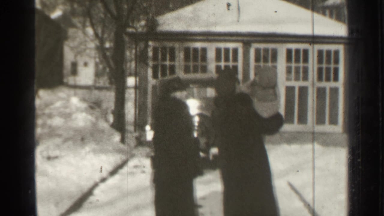 Two bundled adults walk toward a dark car in a snowy driveway.