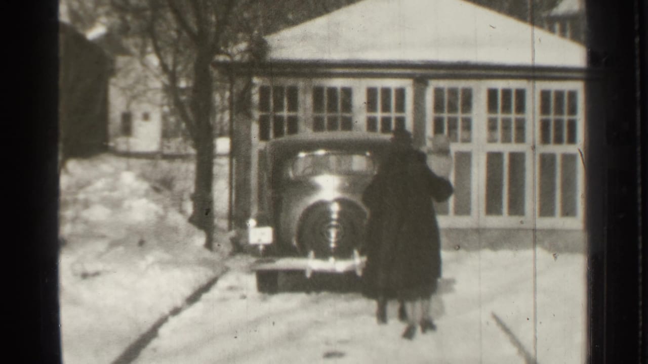 The two adults reach the dark vintage car, seen against snowbanks and a windowed residential exterior in Danielson, Connecticut.