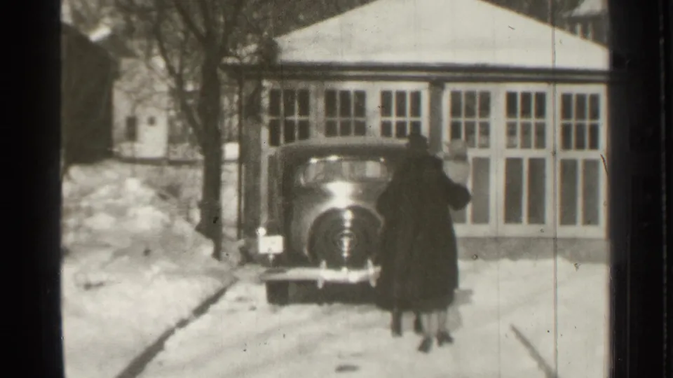 The two adults reach the dark vintage car, seen against snowbanks and a windowed residential exterior in Danielson, Connecticut.