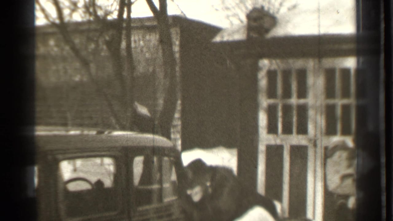 A man stands by an open car door near a snow-covered residential building.