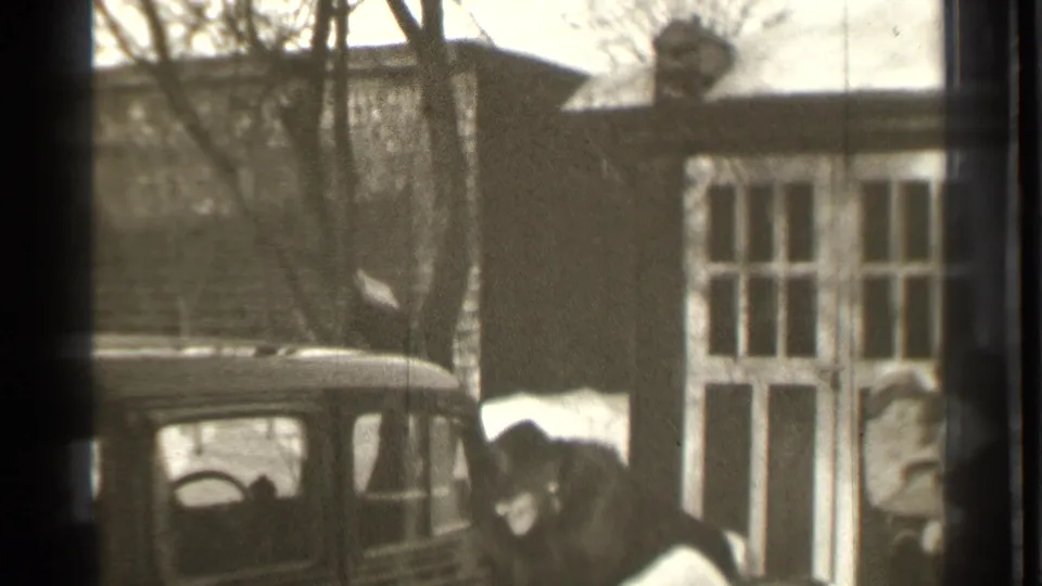A man in a long coat opens a car door beside a parked automobile in the snowy Danielson, Connecticut setting.