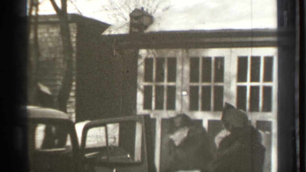 Man in a top hat opens a car door beside a sedan on a residential street.