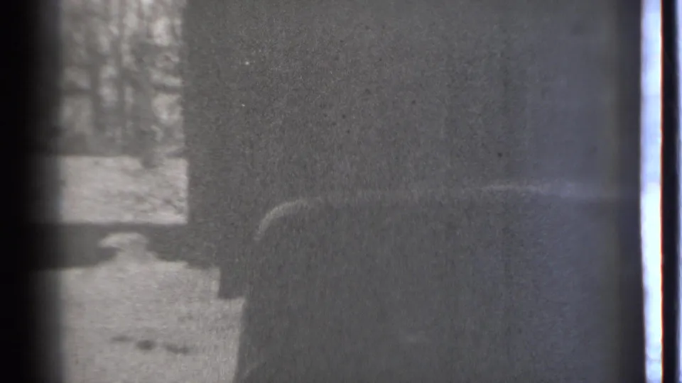 Soft 1939 Connecticut 8mm frame showing snow, tree trunks, and a dark obscured form near a possible doorway or vehicle side.