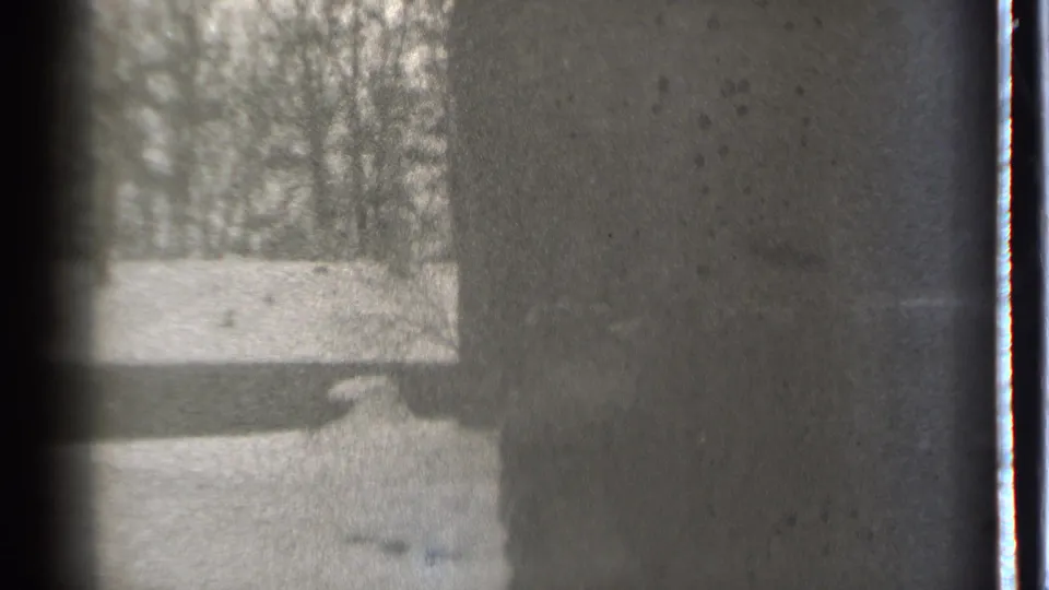 A dim 1939 Danielson frame shows a shadowed figure near a dark wall, with pale ground and bare trees beyond.