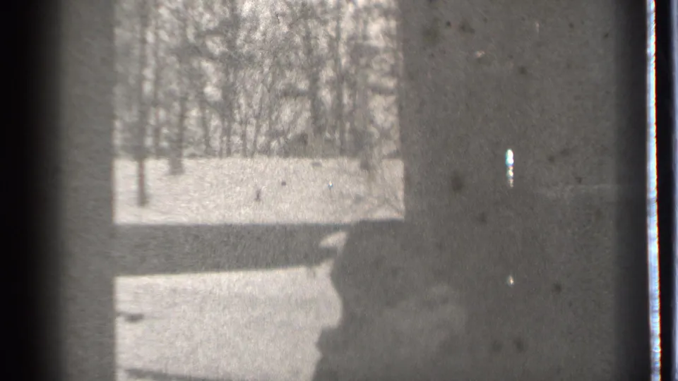Danielson, Connecticut winter home-movie frame with snow, bare trees, and the carried child mostly cropped at the lower right.