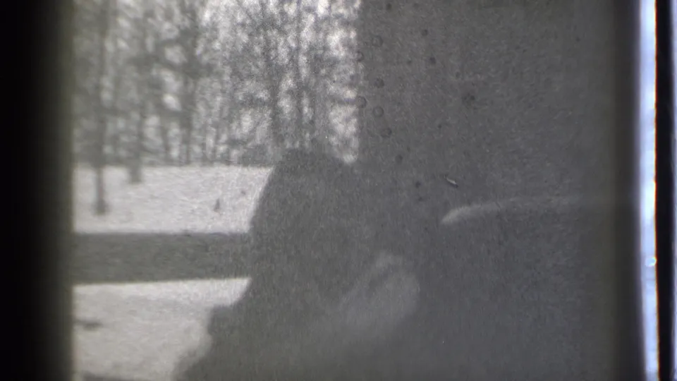 Close 1939 Danielson 8mm frame of a bundled person carrying a child, with snow and bare trees visible behind them.