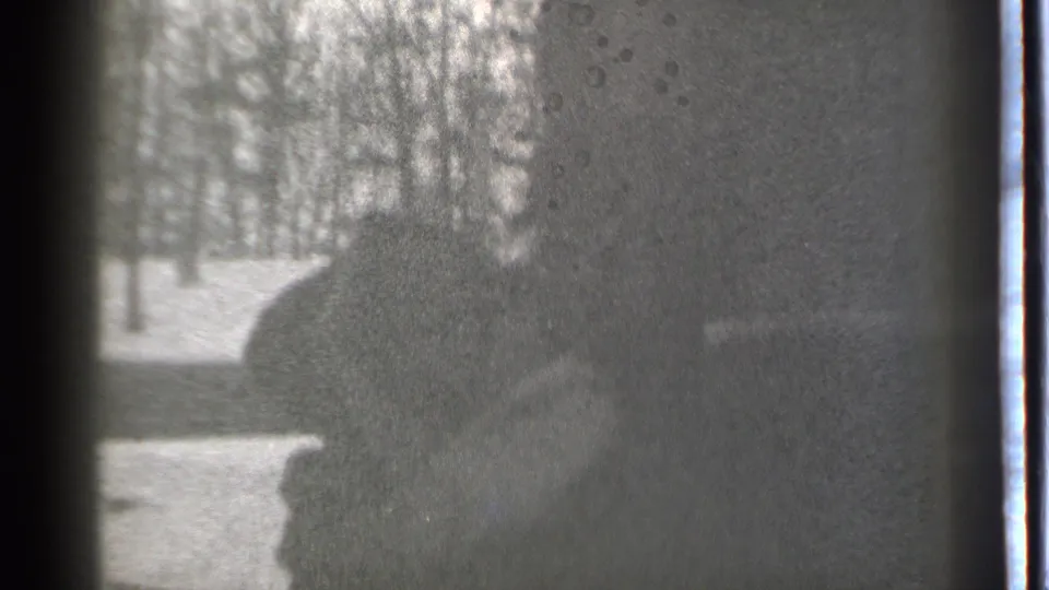 Black-and-white 1939 Danielson home-movie frame showing a silhouetted person by a snowy yard and bare trees, partly obscured by reflections.