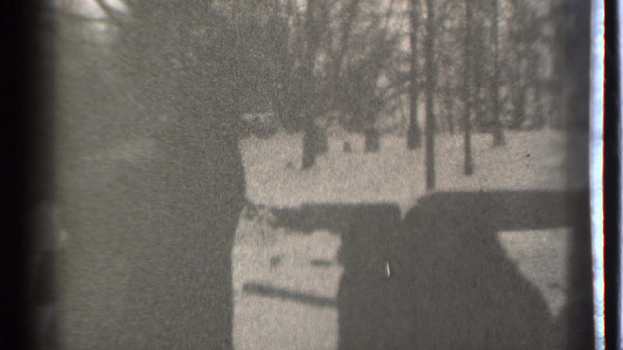 A high-contrast 8mm frame from Danielson, Connecticut, with a shadowed person near snow and winter trees.