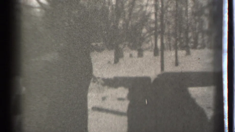 A high-contrast 8mm frame from Danielson, Connecticut, with a shadowed person near snow and winter trees.