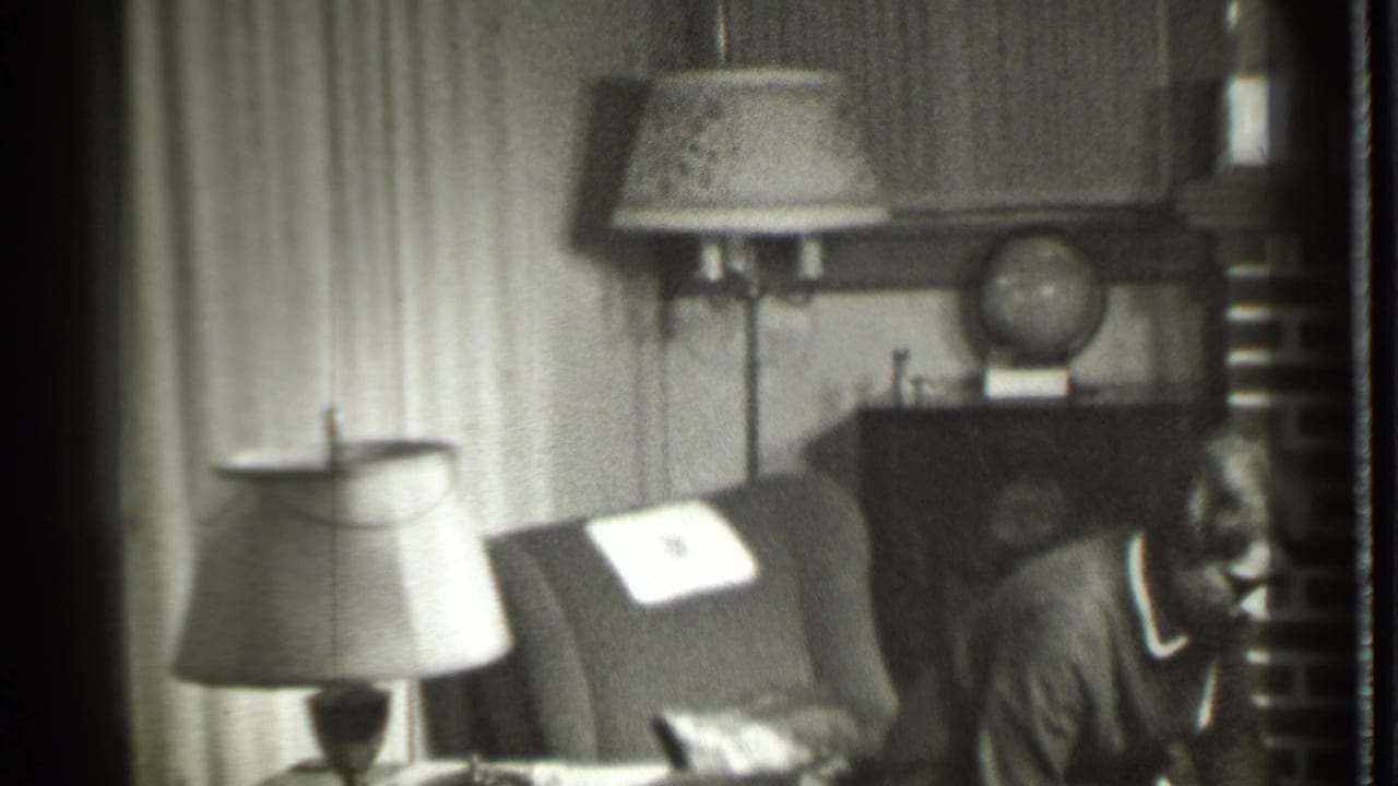 Woman in a robe near a dark armchair in a living room with lamps and curtains.